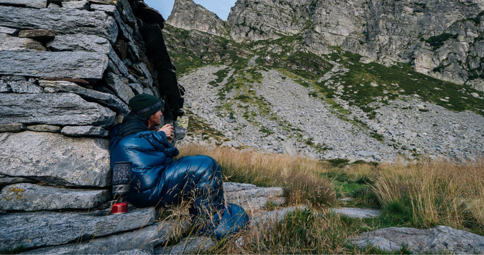 Mann sitzt eingehüllt in Schlafsack an Stein: Schlafsack-Temperaturen