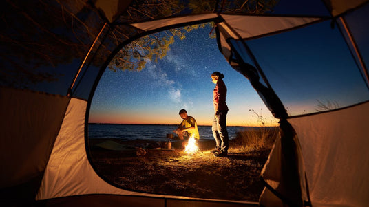 Blick aus einem Zelt auf zwei Personen an einem Lagerfeuer | Camping Ausrüstung mieten