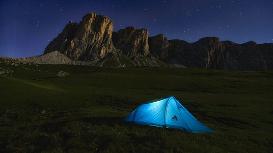 Beleuchtetes Zelt in der Nacht auf einer Weide vor einer Gebirgskette  | Zelte mieten